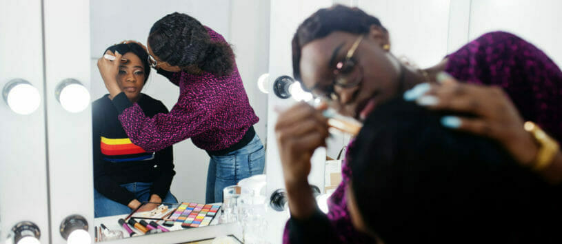 African American woman applying make-up by make-up artist at beauty salon.