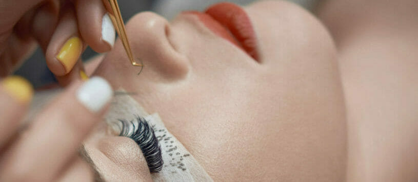 beautician hands with working tools applying false eyelashes to her customer in spa salon, beauty treatment concept.