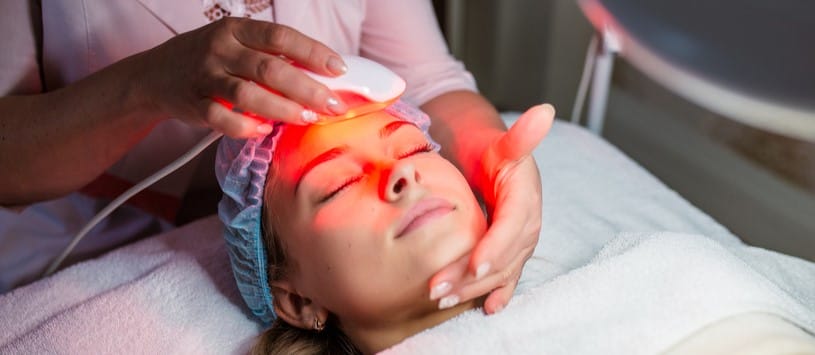 Female client receiving a laser light therapy treatment on her face.